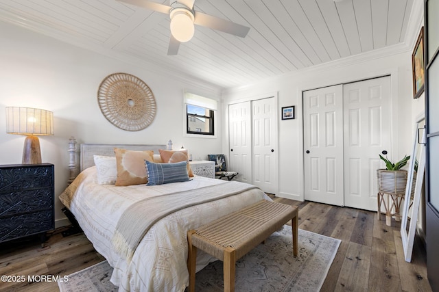 bedroom with wood ceiling, a ceiling fan, crown molding, dark wood-style floors, and multiple closets