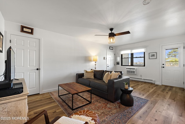 living area with wood-type flooring, baseboards, ceiling fan, a baseboard heating unit, and a wall mounted AC