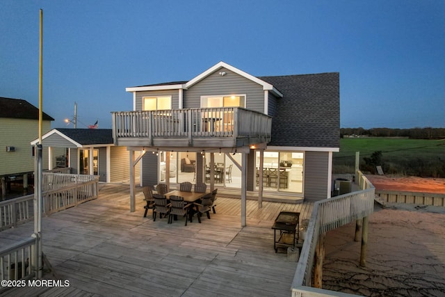 back of property with a shingled roof, outdoor dining area, a deck, and a balcony