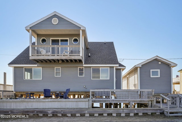 back of property featuring roof with shingles, a wooden deck, and a balcony