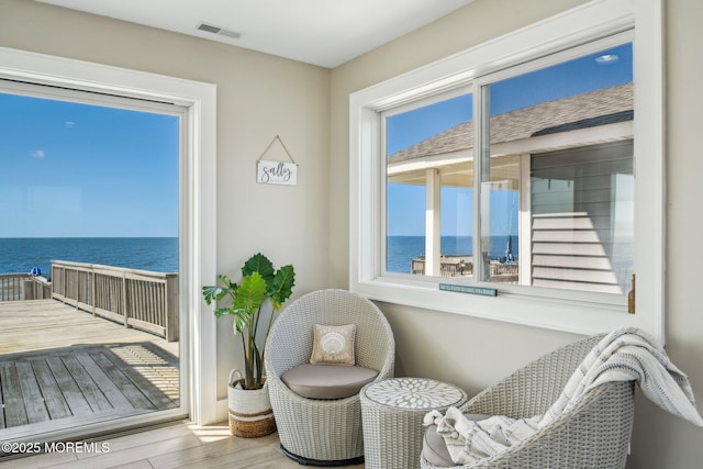sitting room featuring a water view, visible vents, and wood finished floors