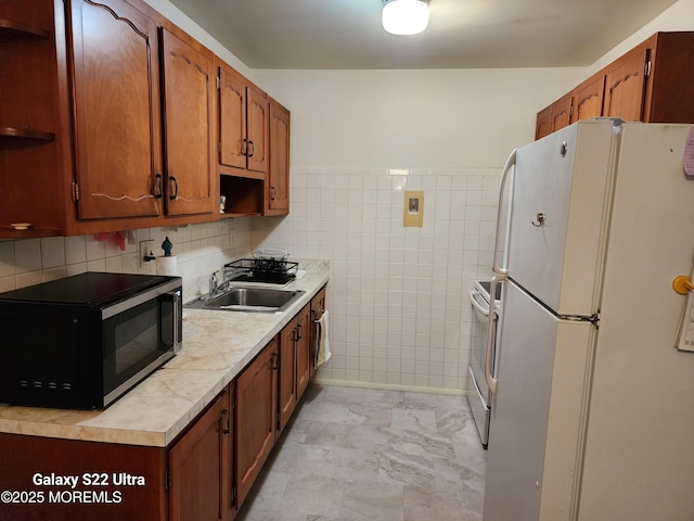 kitchen with freestanding refrigerator, black microwave, tile walls, light countertops, and a sink