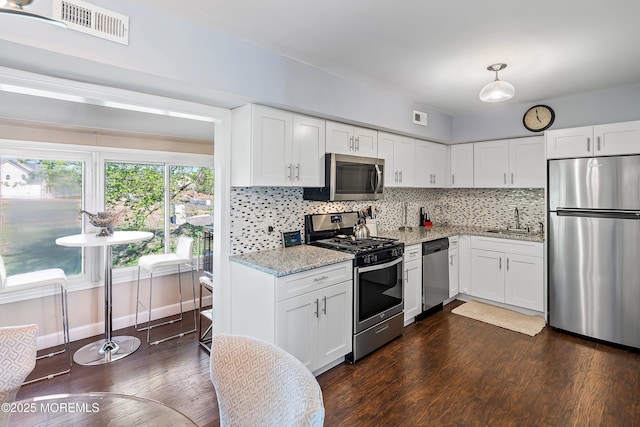 kitchen featuring appliances with stainless steel finishes, light stone counters, a sink, visible vents, and dark wood-style floors