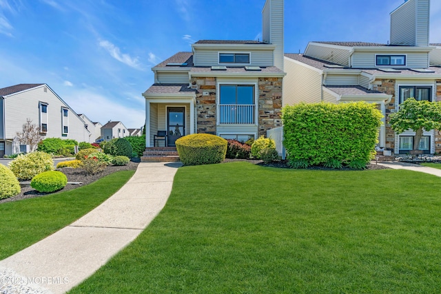 view of front of house featuring a chimney, a shingled roof, stone siding, and a front lawn