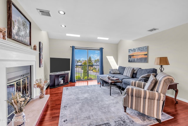 living room with recessed lighting, visible vents, a glass covered fireplace, and wood finished floors