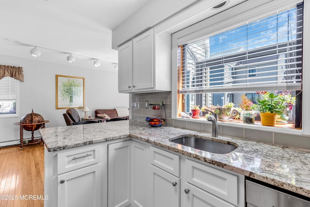 kitchen with decorative backsplash, a peninsula, white cabinetry, light stone counters, and a sink