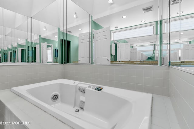 bathroom with tile walls, a tub with jets, and visible vents