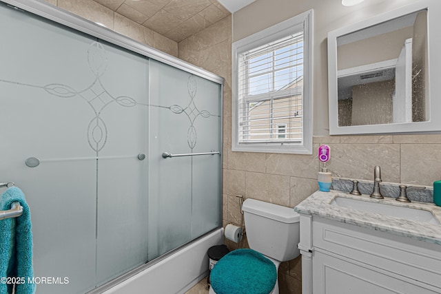 bathroom featuring toilet, tile walls, bath / shower combo with glass door, and vanity