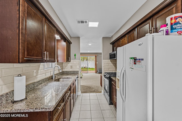 kitchen featuring visible vents, gas range, a sink, stainless steel microwave, and white fridge with ice dispenser