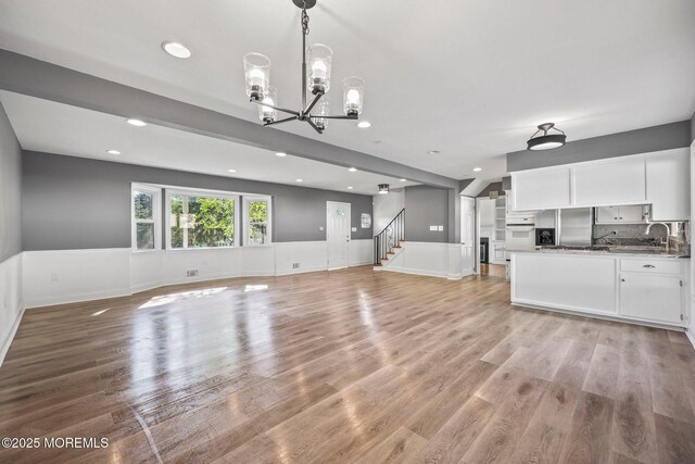 2338 Ramshorn Dr, Allenwood, NJ 08720 - unfurnished living room with a sink, a chandelier, a wainscoted wall, stairs, and light wood-type flooring