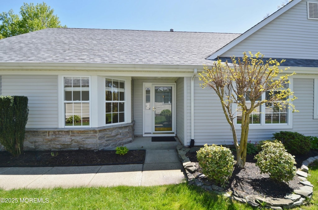 entrance to property with a shingled roof and stone siding