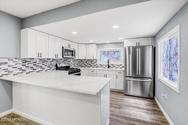 kitchen featuring backsplash, appliances with stainless steel finishes, a sink, a peninsula, and white cabinetry