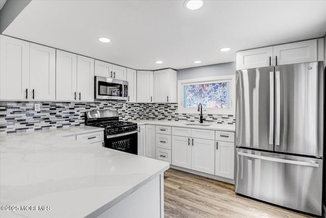 kitchen with light stone counters, a sink, stainless steel appliances, white cabinetry, and light wood-type flooring