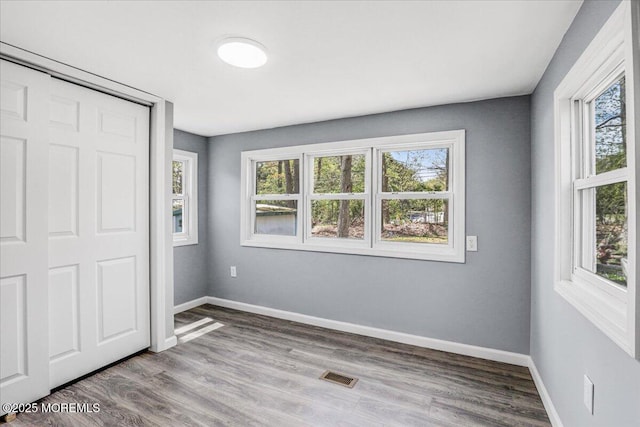 unfurnished bedroom with baseboards, visible vents, wood finished floors, and a closet