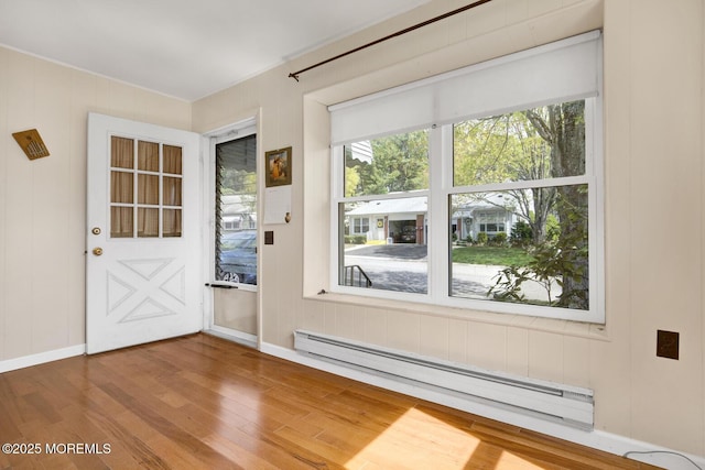 doorway with baseboards, ornamental molding, baseboard heating, and wood finished floors