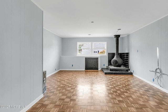 unfurnished living room featuring a wood stove, baseboards, crown molding, and radiator