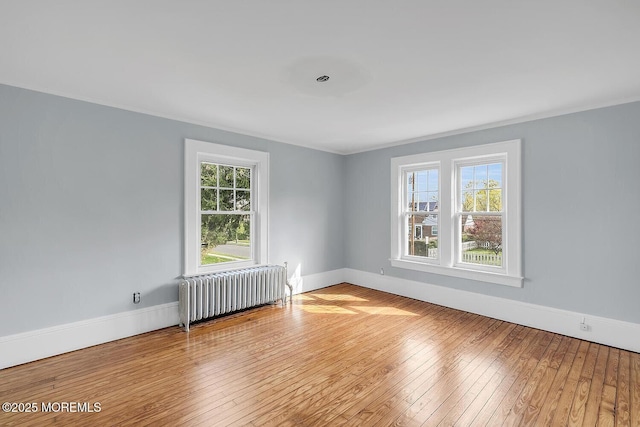 unfurnished room featuring plenty of natural light, radiator, and hardwood / wood-style floors