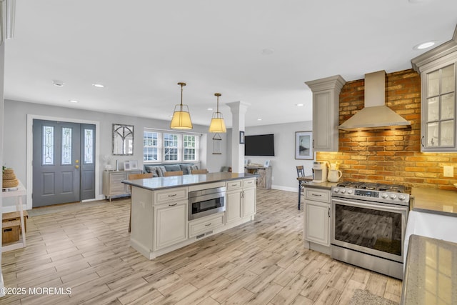 kitchen featuring wall chimney range hood, decorative light fixtures, baseboards, light wood finished floors, and stainless steel appliances