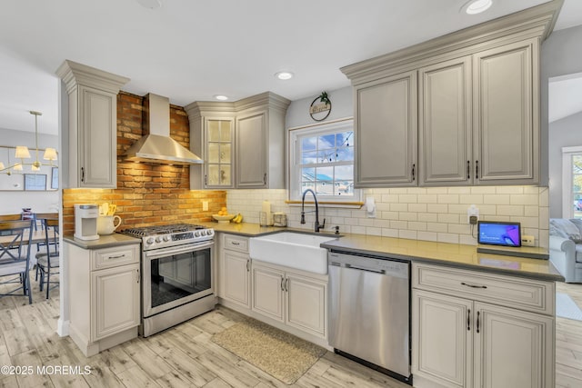 kitchen with a sink, wall chimney exhaust hood, appliances with stainless steel finishes, and cream cabinets
