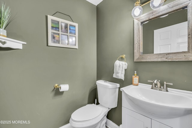 half bathroom with toilet, baseboards, and vanity