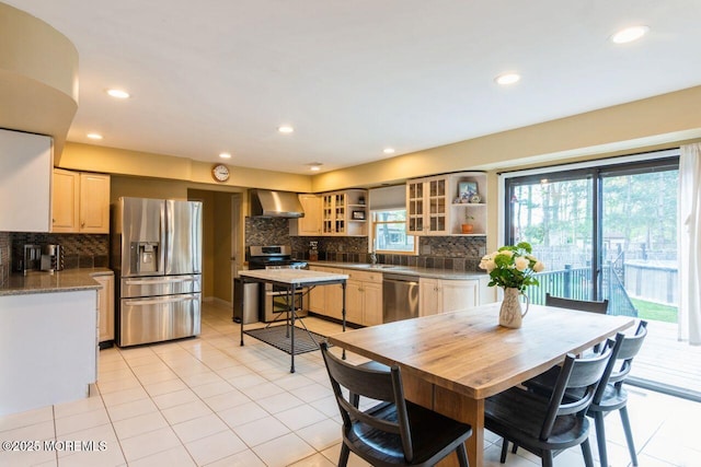 kitchen featuring light tile patterned flooring, light brown cabinets, wall chimney range hood, tasteful backsplash, and appliances with stainless steel finishes