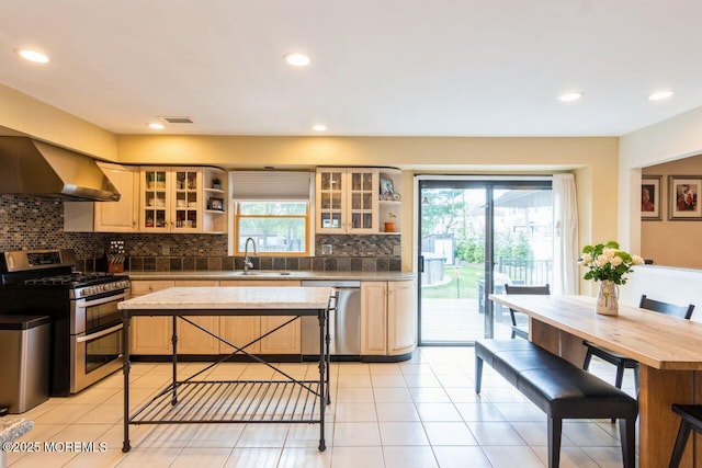 kitchen featuring wall chimney range hood, appliances with stainless steel finishes, backsplash, and a healthy amount of sunlight