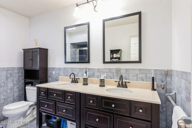 full bathroom featuring a sink, a wainscoted wall, toilet, and tile walls