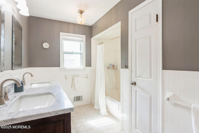 bathroom with a sink, tile walls, a wainscoted wall, and visible vents