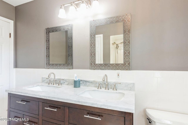 bathroom featuring double vanity, toilet, tile walls, and a sink