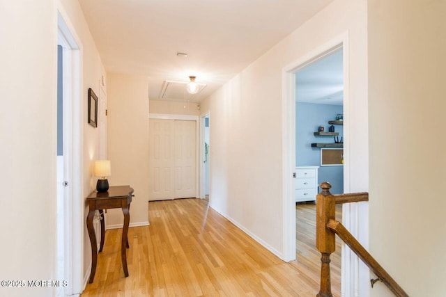 hall featuring light wood-style floors, baseboards, attic access, and an upstairs landing