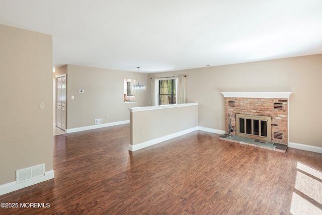 unfurnished living room with baseboards, a brick fireplace, visible vents, and wood finished floors