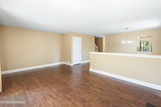 spare room with baseboards, dark wood-style flooring, and a chandelier