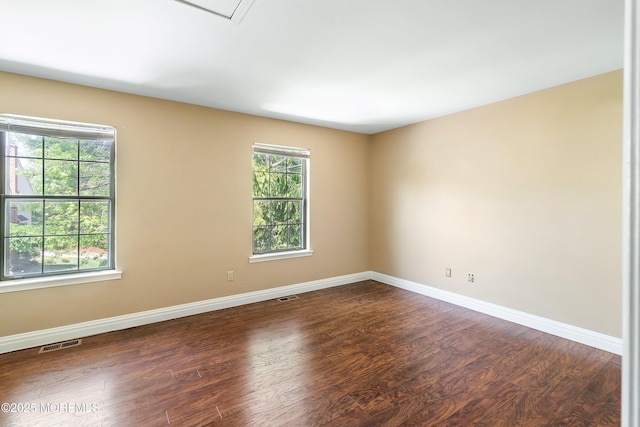 empty room featuring dark wood-style flooring, baseboards, and visible vents
