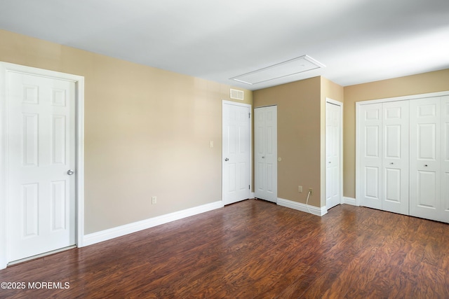 unfurnished bedroom featuring attic access, visible vents, multiple closets, dark wood finished floors, and baseboards