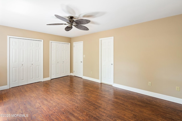 unfurnished bedroom with two closets, baseboards, and dark wood-style floors