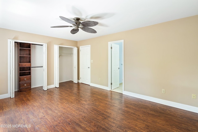 unfurnished bedroom with baseboards, two closets, a ceiling fan, and wood finished floors
