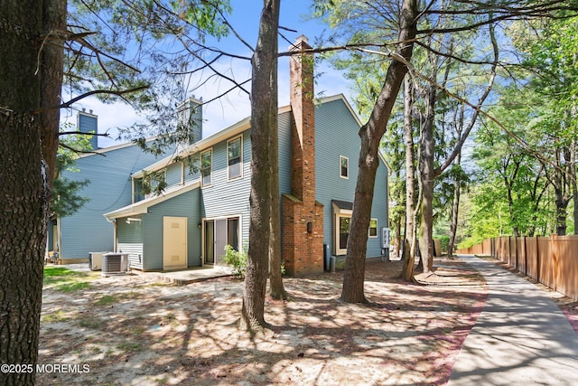 rear view of property with central AC unit, a chimney, and fence