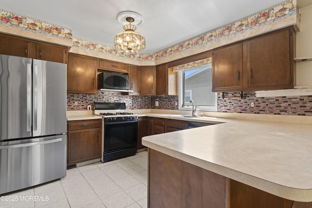 kitchen with freestanding refrigerator, gas range oven, light countertops, tasteful backsplash, and a sink