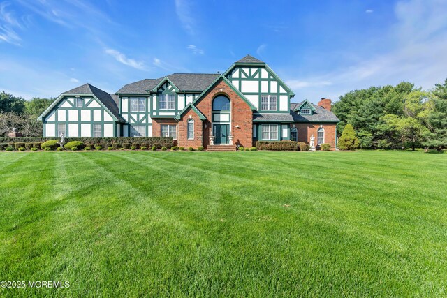 tudor home featuring a chimney, a front lawn, and brick siding