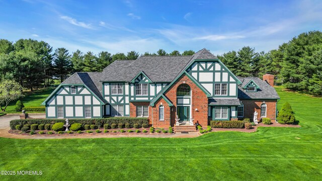 tudor-style house featuring a chimney, a front yard, and brick siding