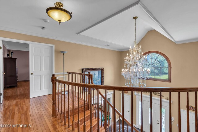 hall with an inviting chandelier, wood-type flooring, crown molding, and an upstairs landing