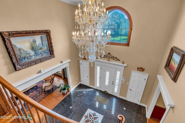 foyer with baseboards, an inviting chandelier, and granite finish floor