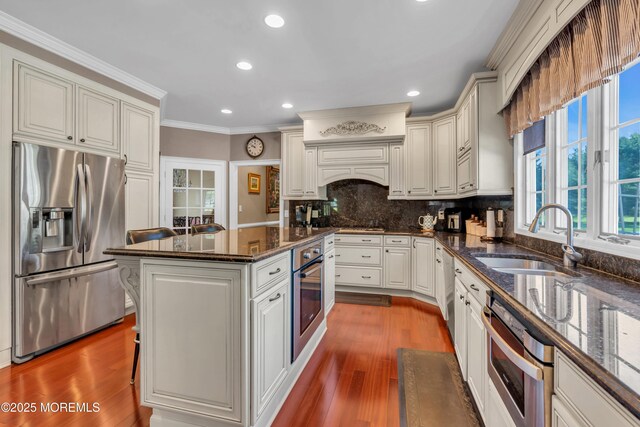 kitchen with appliances with stainless steel finishes, ornamental molding, a sink, and wood finished floors