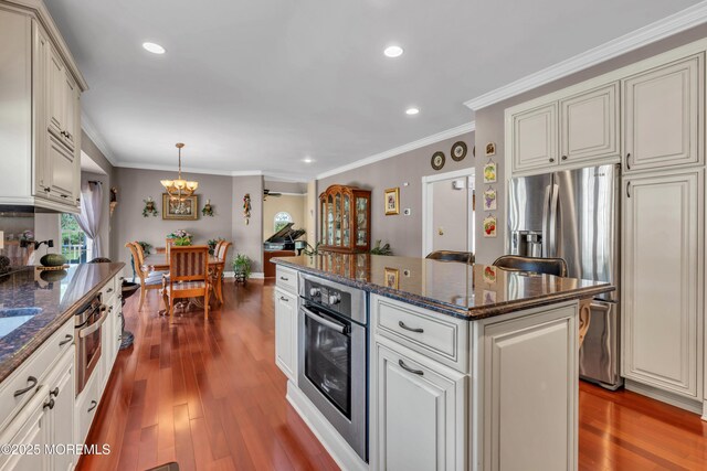 kitchen with wood finished floors, appliances with stainless steel finishes, a kitchen island, and a notable chandelier