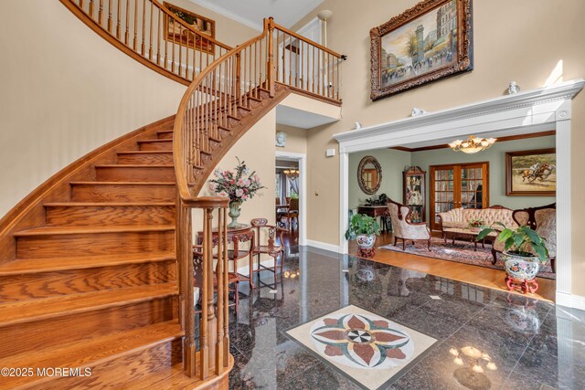 interior space with crown molding, a notable chandelier, granite finish floor, baseboards, and a towering ceiling
