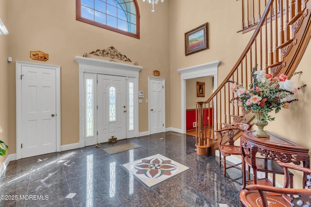 foyer entrance featuring baseboards, granite finish floor, stairs, and a towering ceiling