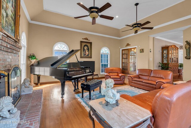 living area featuring baseboards, ceiling fan, a brick fireplace, and wood finished floors