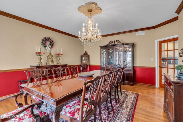 dining space featuring visible vents, crown molding, an inviting chandelier, light wood-style floors, and baseboards