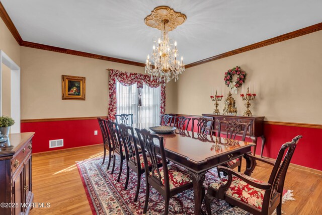 dining room featuring an inviting chandelier, crown molding, light wood-style floors, and visible vents