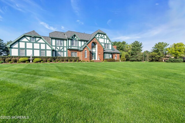 tudor-style house with brick siding, a front lawn, and stucco siding